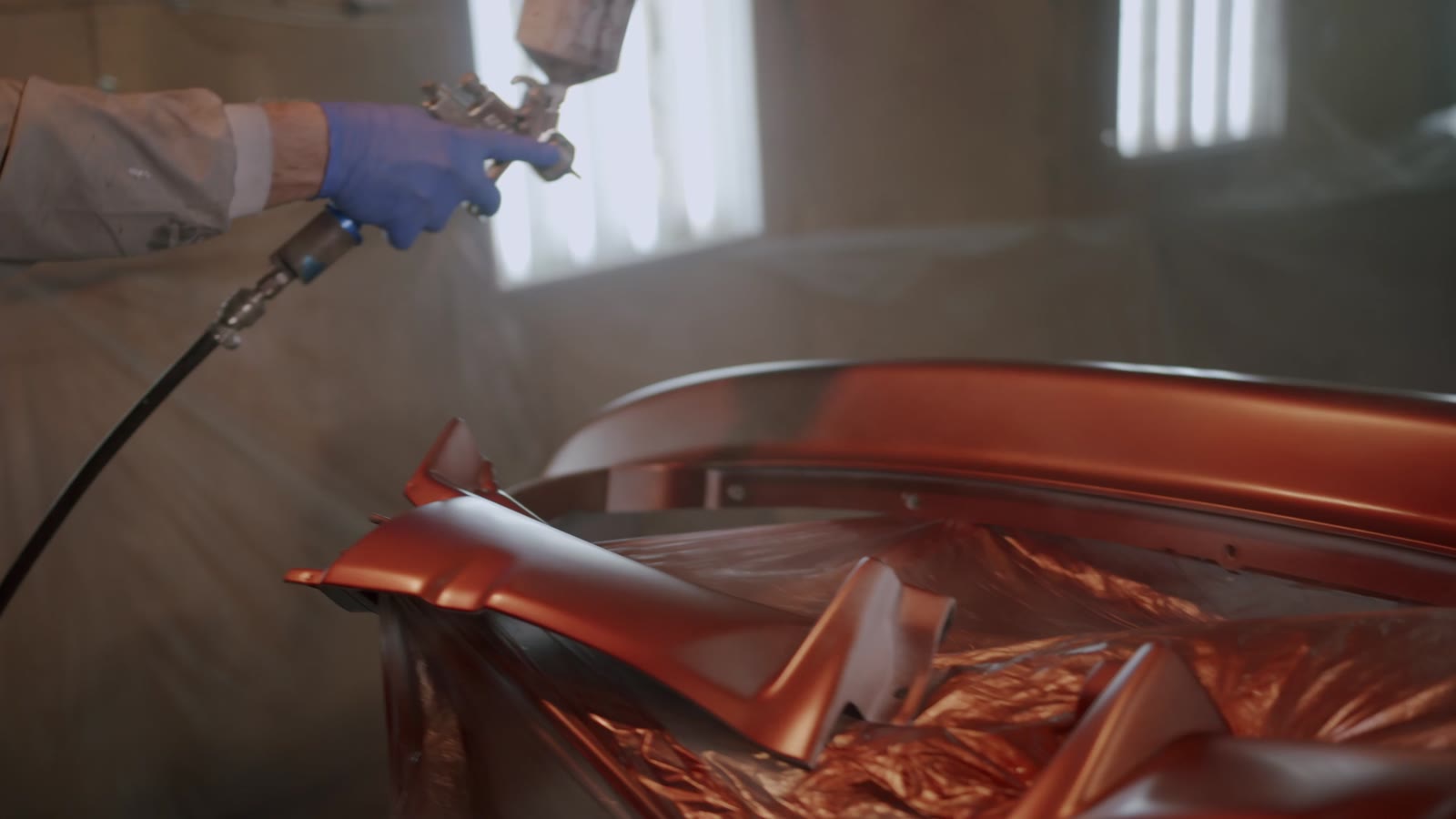 Mains gantées appliquant la peinture au pistolet sur des pièces de carrosserie